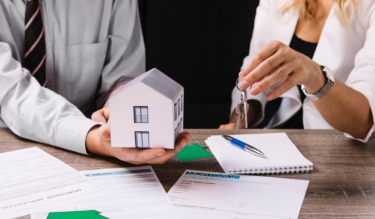 Close-up of a real estate or mortgage transaction showing one person handing over house keys while another holds a miniature home model.
