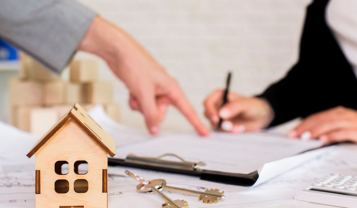 Close-up real estate concept image featuring a small wooden house model and house keys placed on top of property documents.